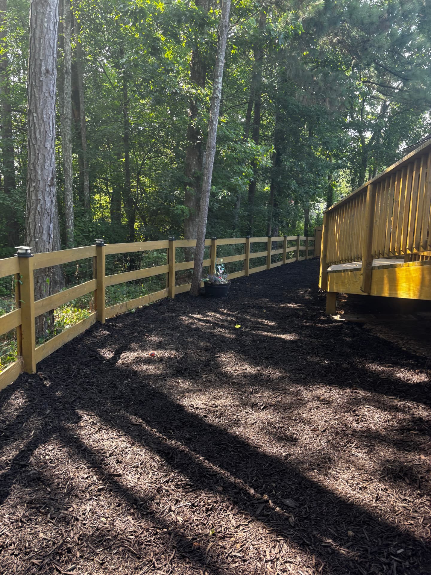 Shaded mulched yard along a wood rail fence and deck