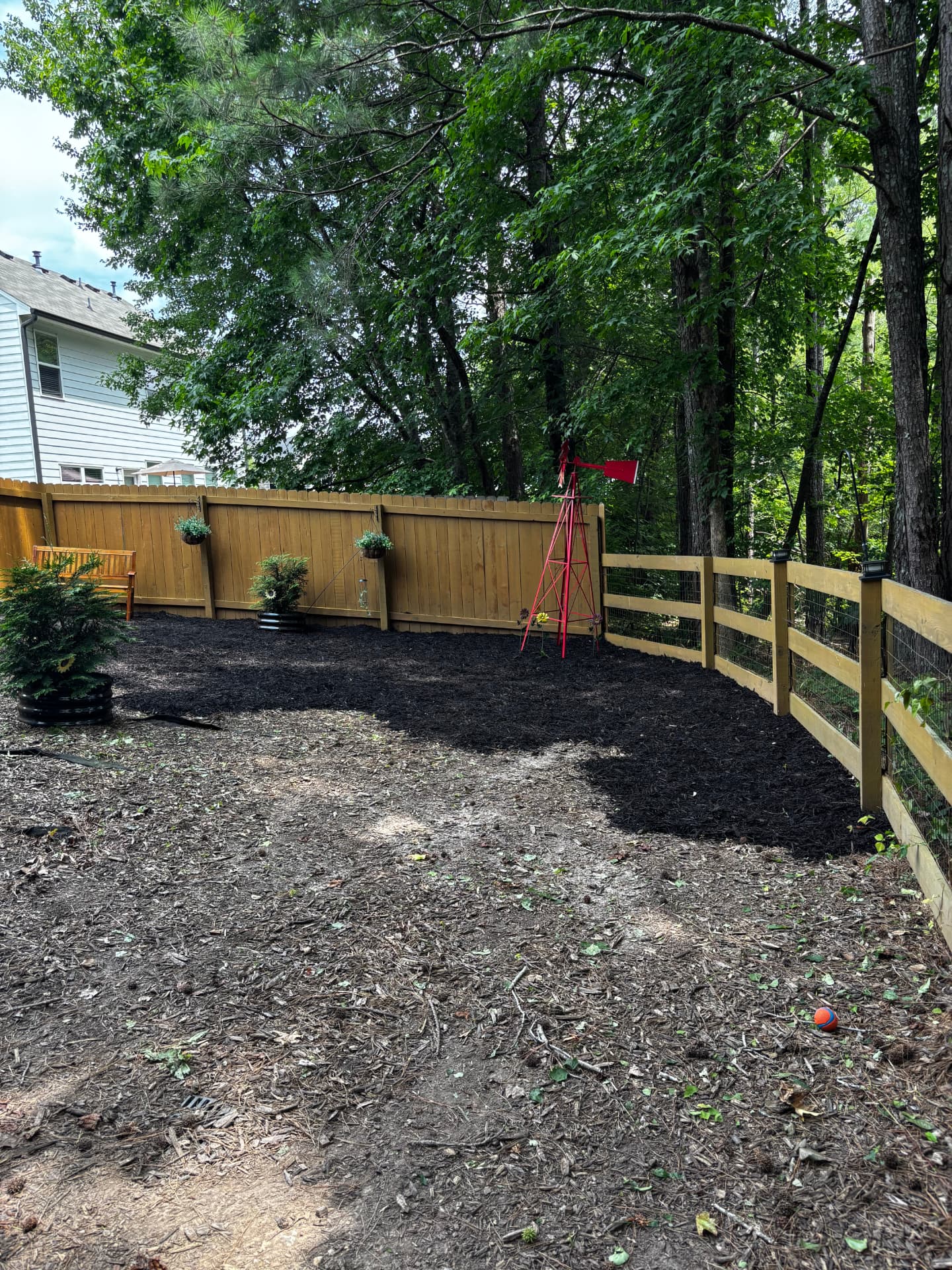 Mulch bed with shrubs and a decorative windmill along the fence line